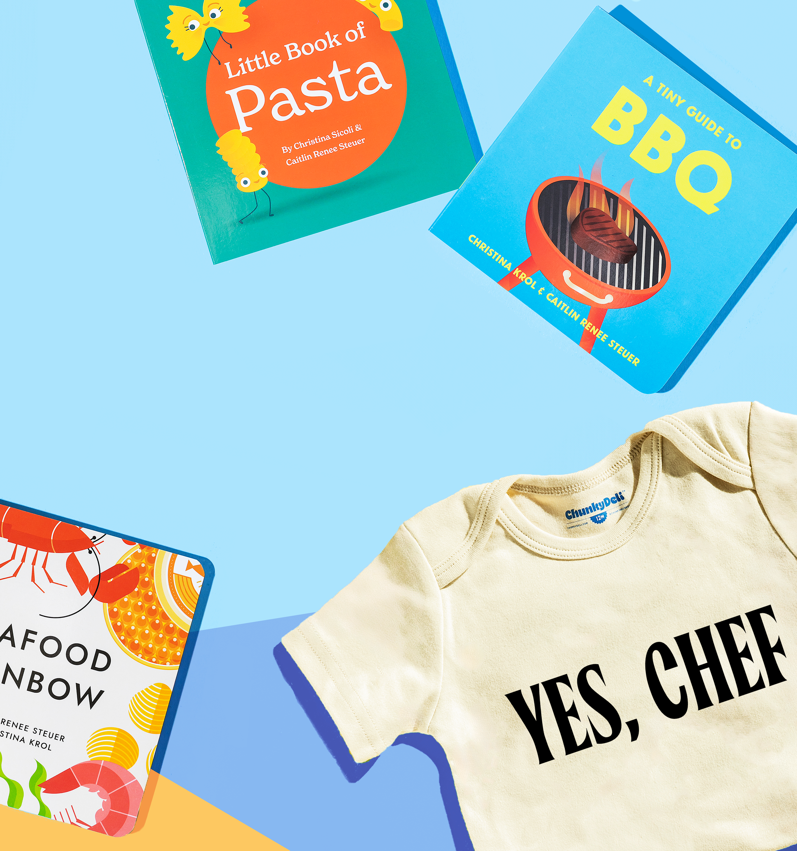 Three different books, "Little Book of Pasta," "A Tiny Guide to BBQ," and "Seafood Rainbow," along with a "YES, CHEF" onesie, are laid out on a light blue surface.
