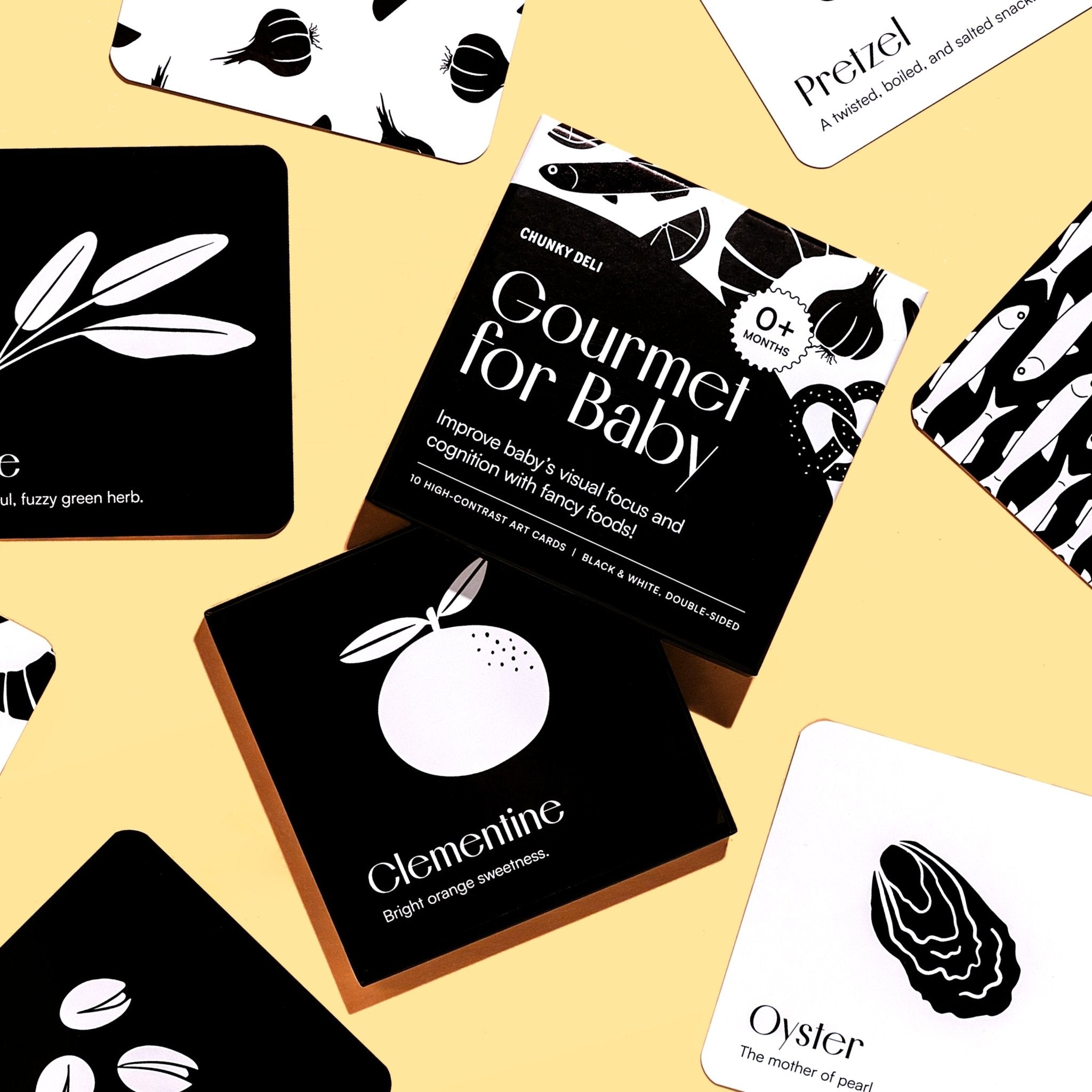 Top-down flat lay of the "Gourmet for Baby" art cards, with the box in the center, on a pastel yellow surface.