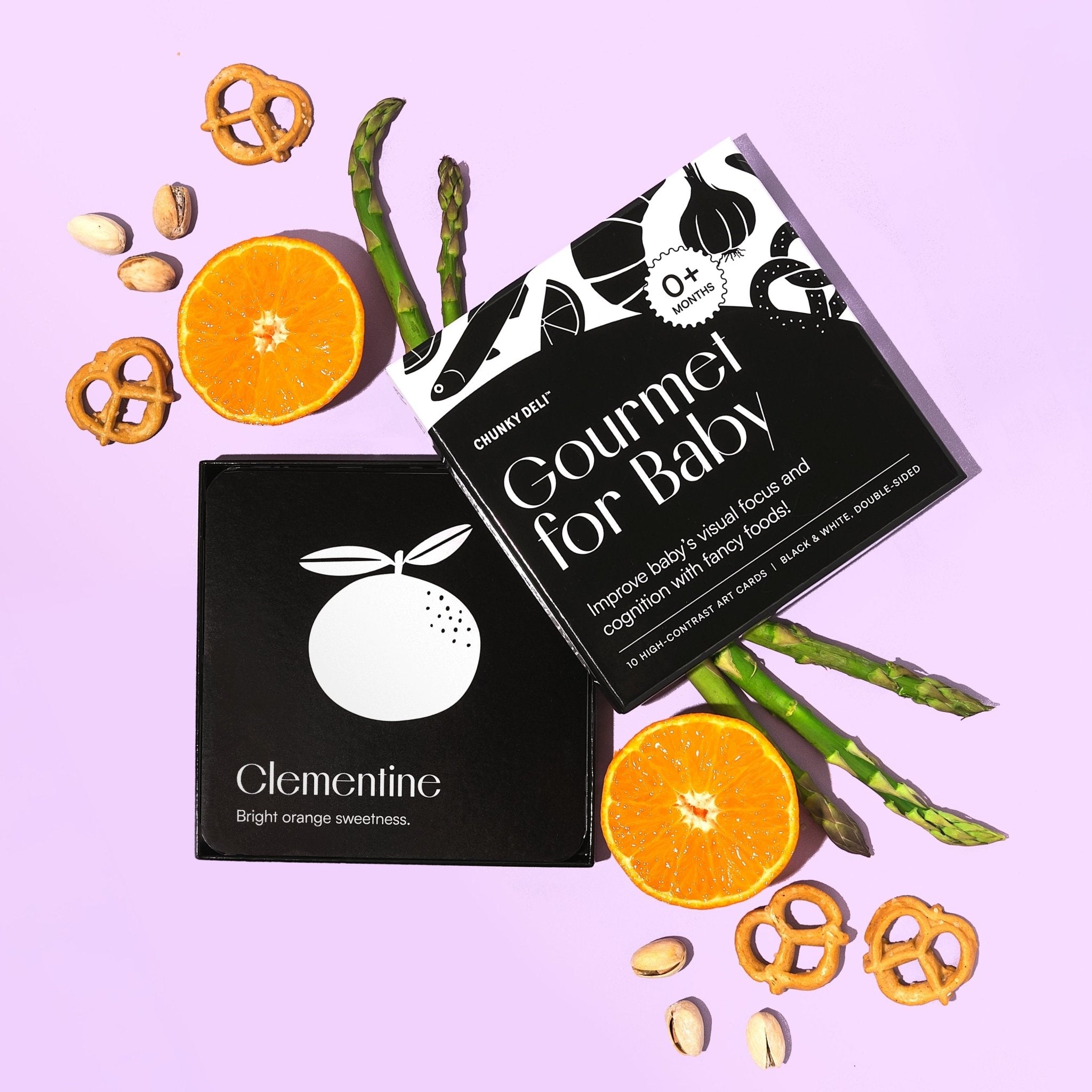 Top-down product shot of the "Gourmet for Baby" art cards, with oranges, pistachios, pretzels, and asparagus.