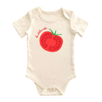 Chunky Deli baby bodysuit made from 100% cotton, short sleeve, beige/natural color featuring a large red tomato graphic and the words 'La Dolce Vita' printed across the chest. Includes envelope neckline and snap closure.