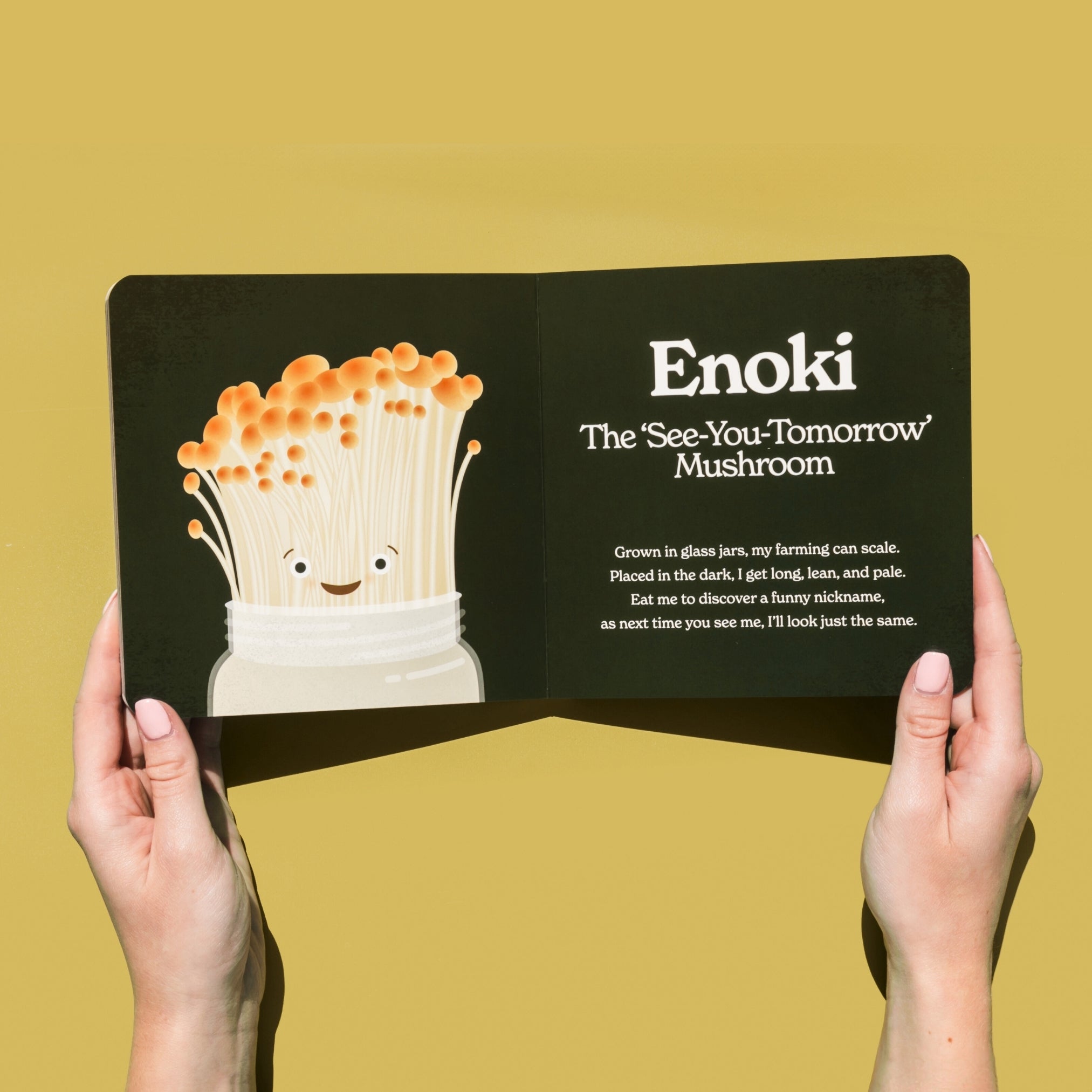 Chunky Deli product image: "Little Book of Fungi" open to the Enoki mushroom page (dark green spread), featuring an illustration of the Enoki mushroom character, held by two hands against a pale yellow/green background.