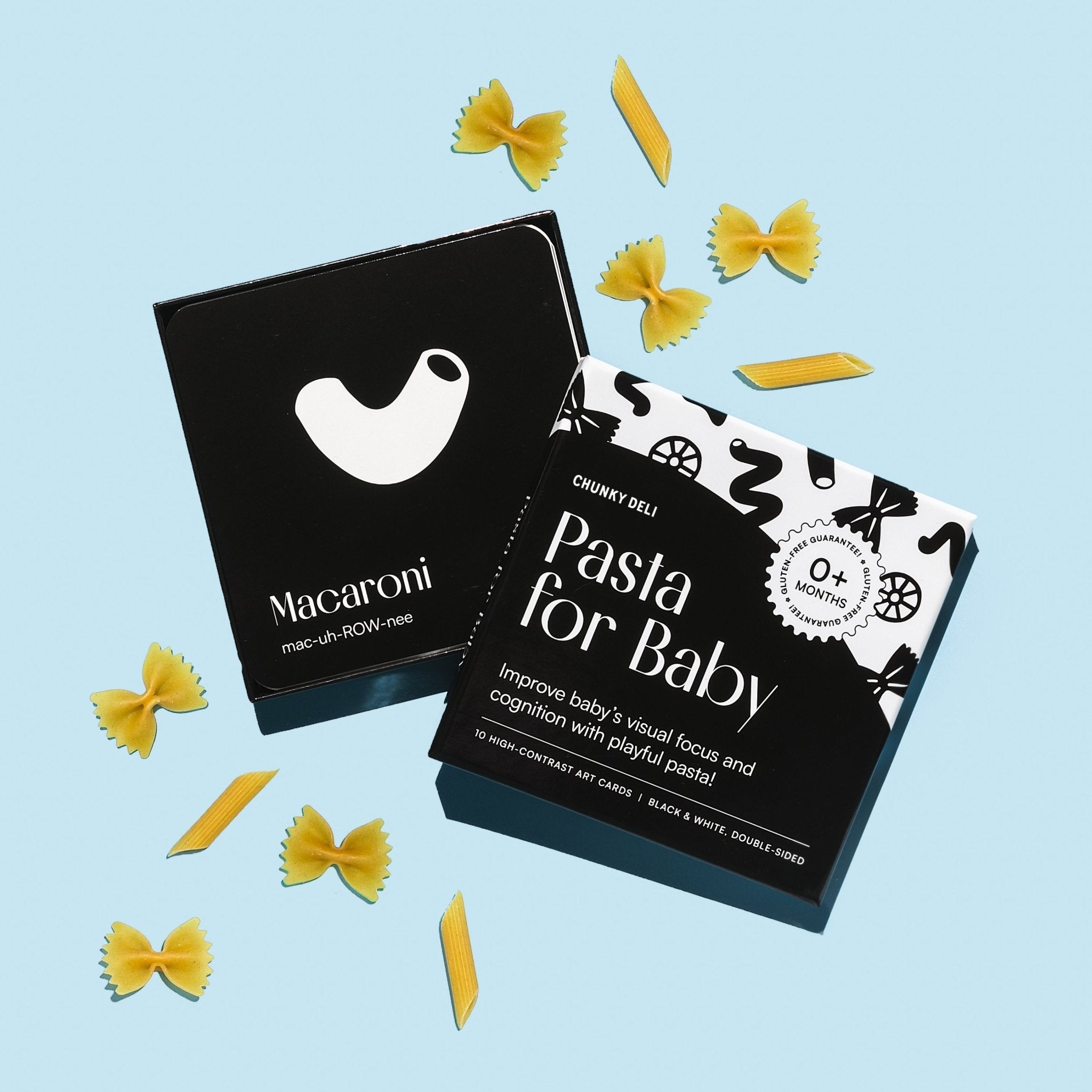 Top-down product shot of the "Pasta for Baby" art cards, with bow tie and penne pasta scattered around.