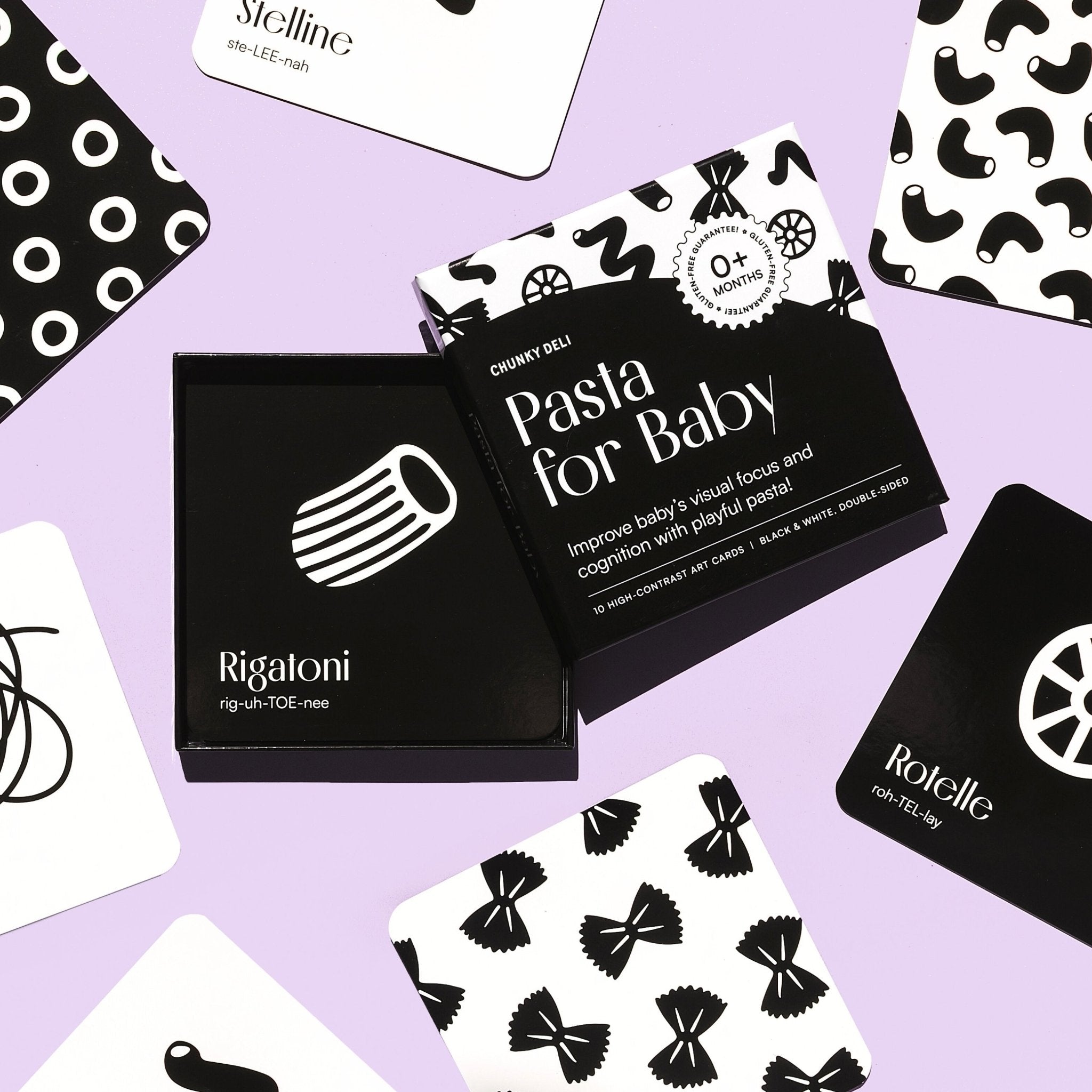 Top-down flat lay of the "Pasta for Baby" art cards, with the box in the center, on a pastel purple surface.