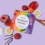 Chunky Deli "Rainbow Books Fancy Flavors Collection" slipcase, designed with a vibrant rainbow of food illustrations, surrounded by various food-related props including a lobster claw, salmon caviar, sliced lemons, tomatoes, vanilla beans, cinnamon sticks