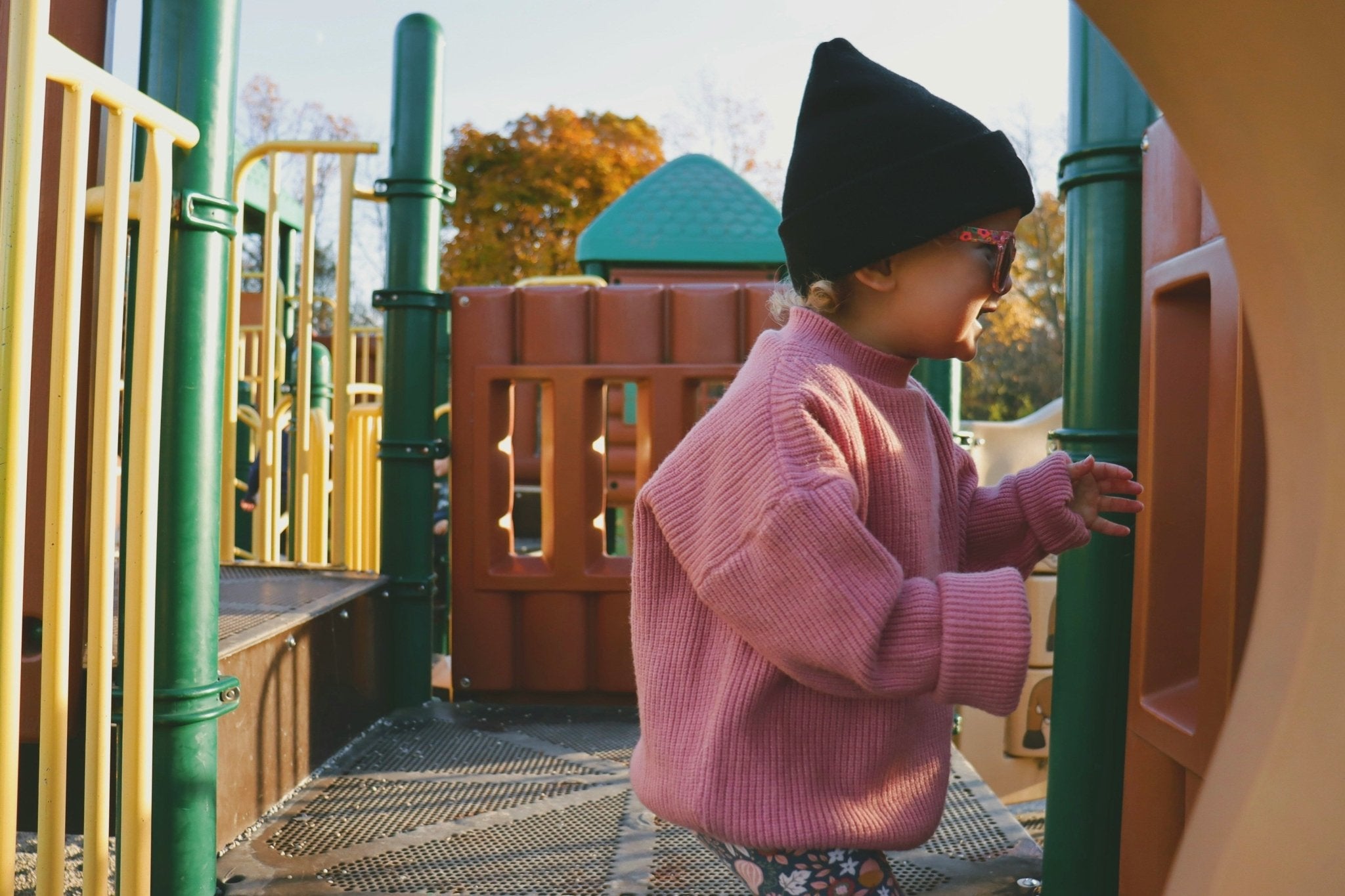 Young girl on a playset in a sweater and beanie. Photo by Shaylyn on Unsplash.