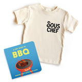 Chunky Deli 'BBQ Baby Starter Pack' featuring a beige, 100% cotton, short sleeve toddler tee with black 'Sous Chef' text and 'A Tiny Guide to BBQ' 6x6 inch, 18-page board book by Christina Krol and Caitlin Renee Steuer.
