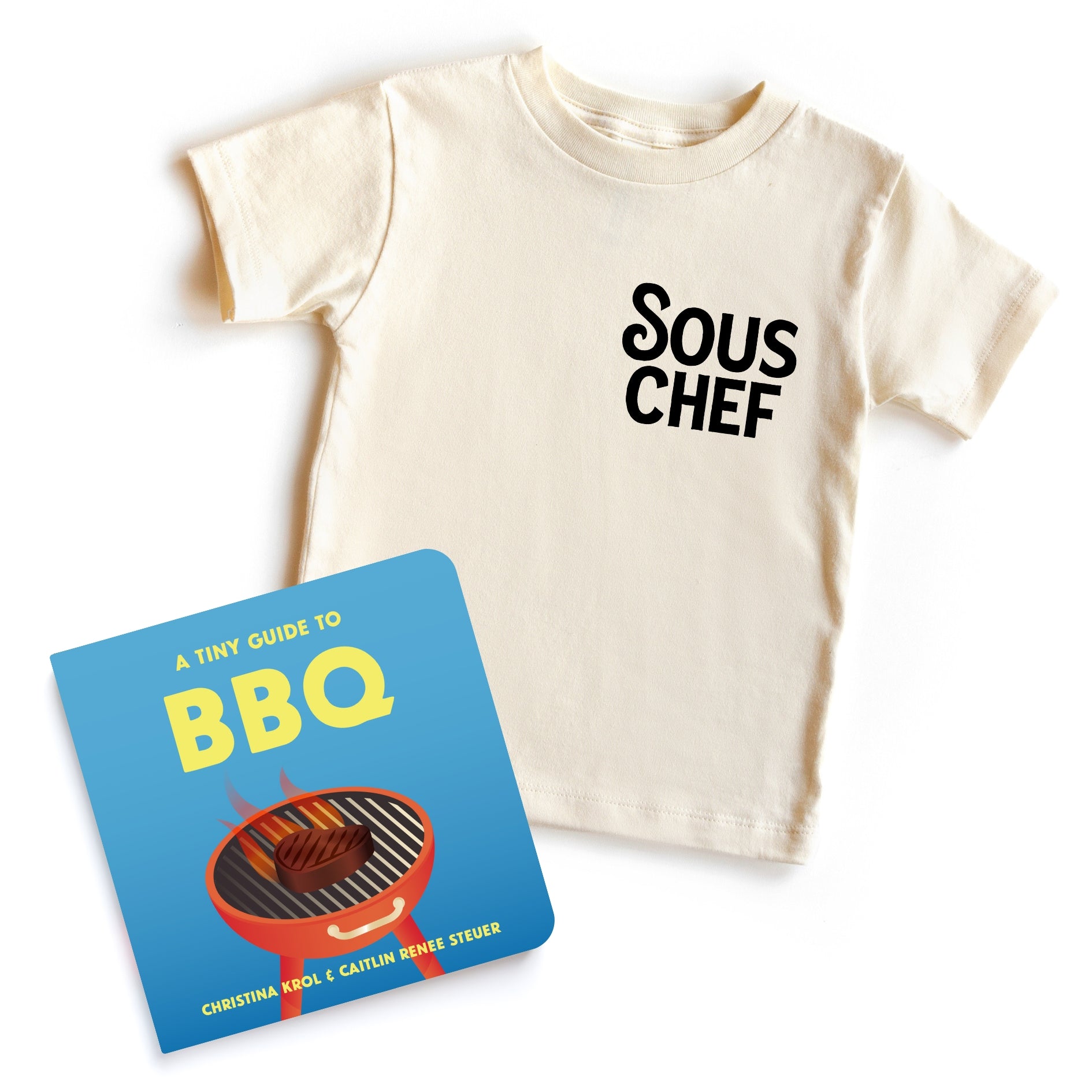 Chunky Deli 'BBQ Baby Starter Pack' featuring a beige, 100% cotton, short sleeve toddler tee with black 'Sous Chef' text and 'A Tiny Guide to BBQ' 6x6 inch, 18-page board book by Christina Krol and Caitlin Renee Steuer.
