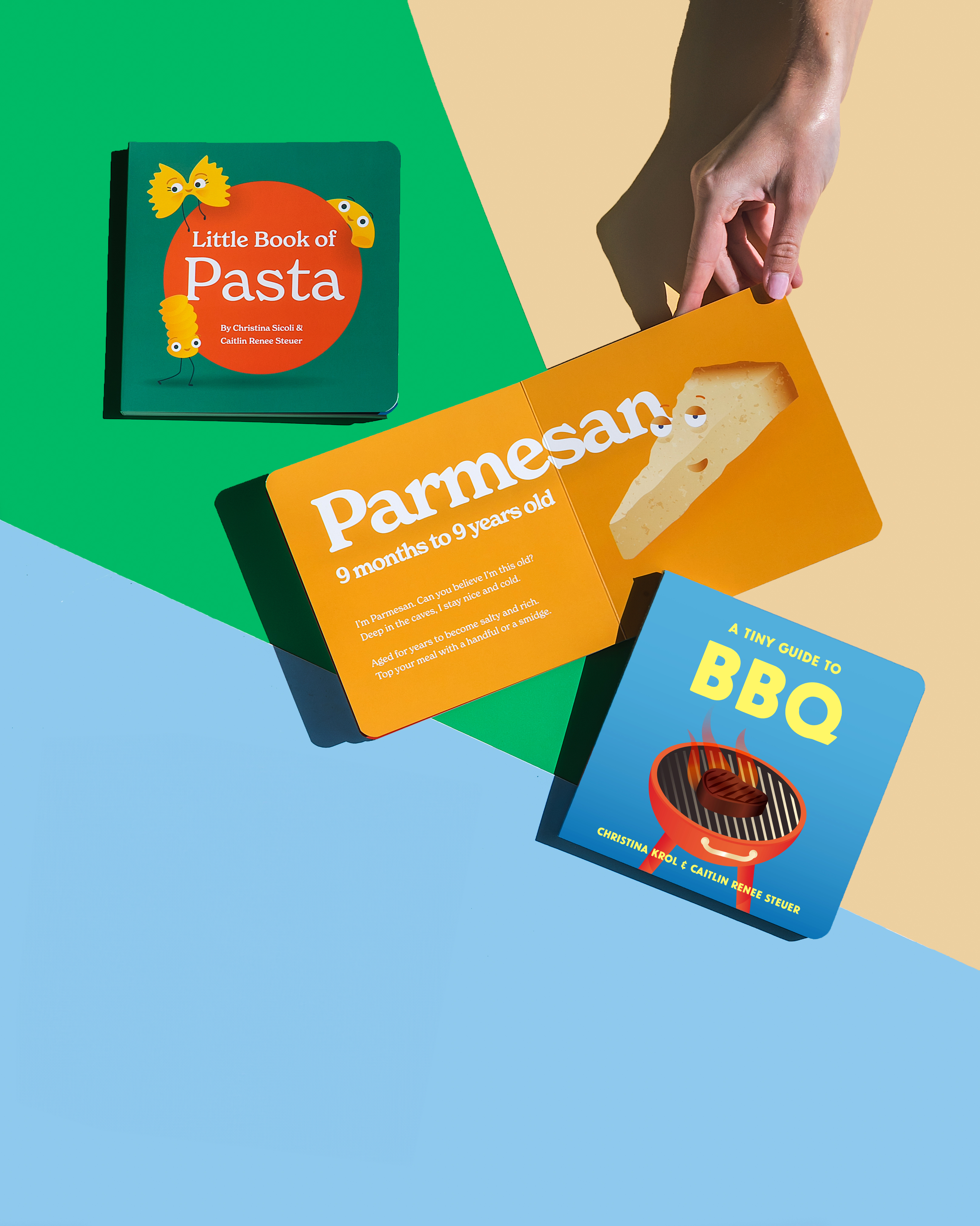 A hand holds open the book "Little Book of Cheese" on a green and blue background. The book is open to a vibrant orange-colored page that features an illustration of a wedge of Parmesan cheese. "Little Book of Pasta" and "A Tiny Guide to BBQ" are also on the surface.