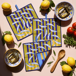 Chunky Deli product image of three kitchen towels with fish pattern on a white table with anchovies, lemon and other kitchen goods. 