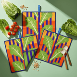 Chunky Deli lifestyle image of colorful kitchen towels with leaf pattern on a green table with vegetables and salad forks.