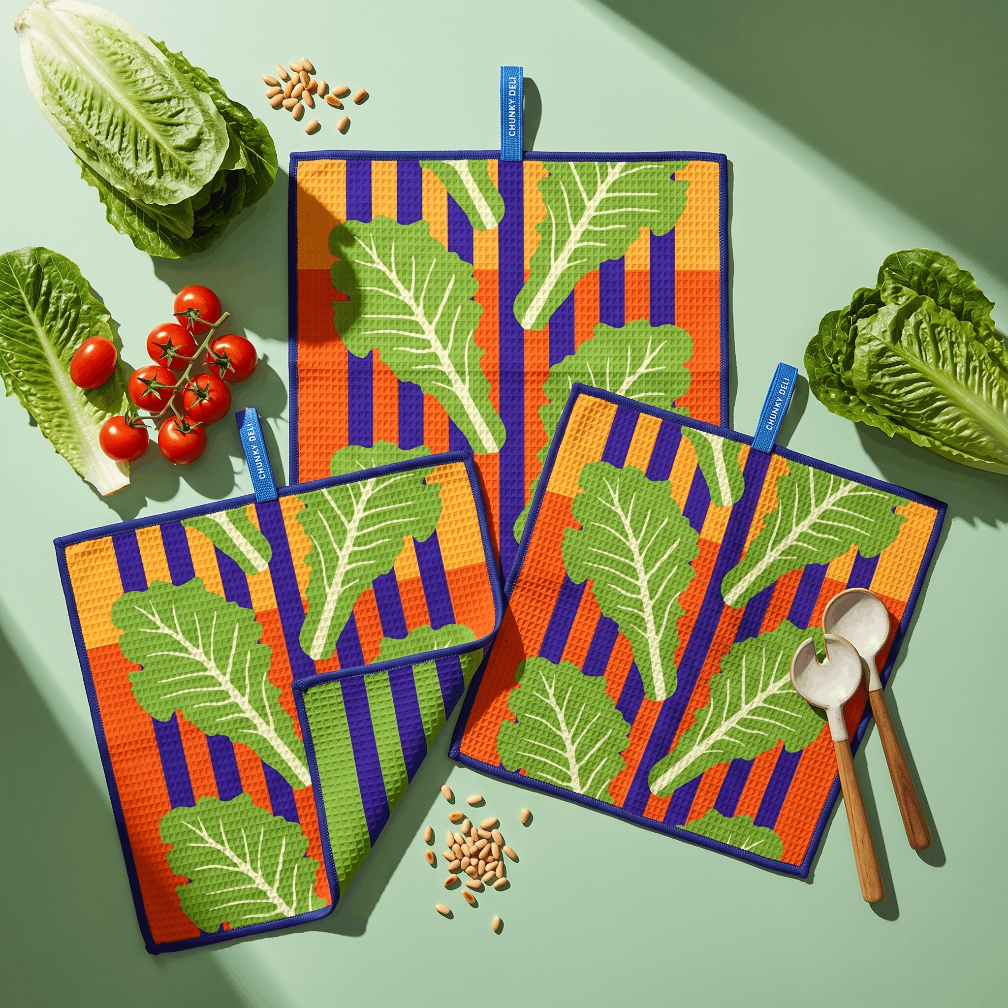 Chunky Deli lifestyle image of colorful kitchen towels with leaf pattern on a green table with vegetables and salad forks.