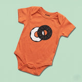 Chunky Deli Product Image: Orange baby onesie with a two tone graphic of an everything bagel with cream cheese on a green background