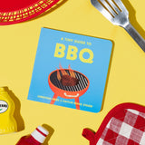 A Tiny Guide to BBQ book cover, on a yellow background with a red basket, mustard, ketchup, grill spatula, and oven mitt. From Chunky Deli Written by Christina Krol & Caitlin Renee Steuer