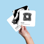 Hand holding three Chunky Deli black and white baby art cards featuring toast and waffles against a light blue background.