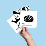 Hand holding three Chunky Deli black and white baby art cards featuring a patty and ketchup against a light blue background.