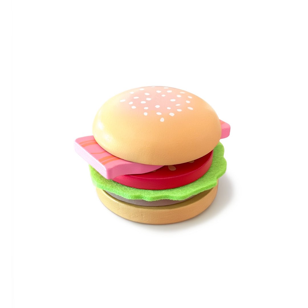 multi-layered toy hamburger from the Chunky Deli range. The stack, from top to bottom, features a light-brown wooden bun top with painted white sesame seeds, a wavy green felt lettuce leaf, a thick red wooden tomato slice, a rectangular pink wooden block representing bacon with dark stripes, a dark-brown wooden meat patty, and a light-brown wooden bun base