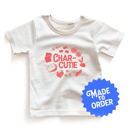 Chunky Deli product image: White short-sleeved kids' and toddler t-shirt with the text "Charcutie" in orange font, surrounded by illustrations of charcuterie board foods, on the chest.