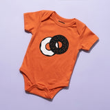 Chunky Deli Product Image: Orange baby onesie with a two tone graphic of an everything bagel with cream cheese on a purple background