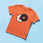 Chunky Deli product image: Toddler tee in 100% cotton, short sleeve, orange color. Features a graphic illustration of everything bagel with cream cheese in 2 colors, black and white, centered on the chest on a blue background.