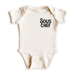 Chunky Deli product image: Natural-colored "Sous Chef" bodysuit (100% cotton) laid flat on a white background, showcasing the envelope shoulders and three-snap closure.