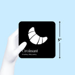 Gloved hand holds a black and white "Croissant" art card, showing its 5-inch size on a blue background from the Gourmet for Baby art cards from Chunky Deli.