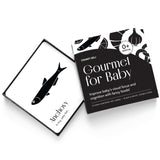 High-angle product shot of a black and white "Gourmet for Baby" art card set. An anchovy card rests on the open box.