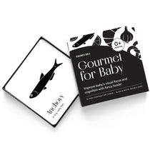 High-angle product shot of a black and white "Gourmet for Baby" art card set. An anchovy card rests on the open box.