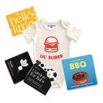 Chunky deli product image of the grillmaster baby bundle, top down view of a baby onesie with a bold graphic and "lil' Slider" Printed in orange font. There is also a tiny guide to BBQ and Garden for Baby art cards. 