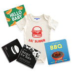 Chunky deli product image of the grillmaster baby bundle, top down view of a baby onesie with a bold graphic and "lil' Slider" Printed in orange font. There is also a tiny guide to BBQ, Burger for Baby art cards and a "Hello Baby" gift note. 