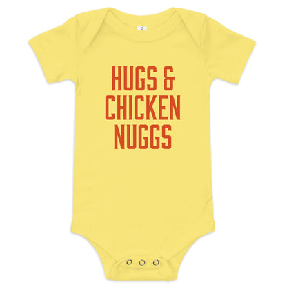 Chunky Deli product image: "Hugs and Chicken Nugs" bodysuit (100% cotton, yellow color) laid flat on a white background, showcasing the envelope shoulders, short sleeves, three-snap closure, and the text "Hugs and Chicken Nugs" in orange font on the chest