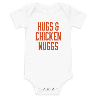 Chunky Deli product image: "Hugs and Chicken Nugs" bodysuit (100% cotton, natural color) laid flat on a white background, showcasing the envelope shoulders, short sleeves, three-snap closure, and the text "Hugs and Chicken Nugs" in orange font on the ches