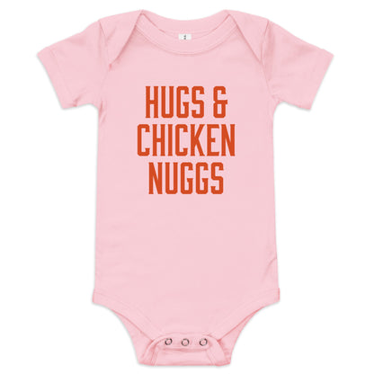 Chunky Deli product image: "Hugs and Chicken Nugs" bodysuit (100% cotton, pink color) laid flat on a white background, showcasing the envelope shoulders, short sleeves, three-snap closure, and the text "Hugs and Chicken Nugs" in orange font on the chest.