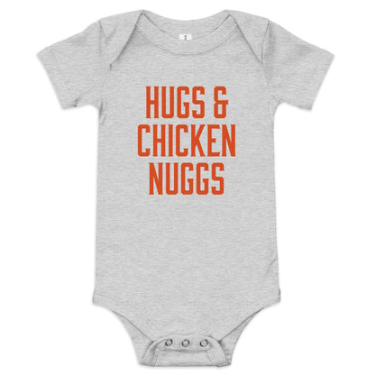 Chunky Deli product image: "Hugs and Chicken Nugs" bodysuit(100% cotton, grey color) laid flat on a white background, showcasing the envelope shoulders, short sleeves, three-snap closure, and the text "Hugs and Chicken Nugs" in orange font on the chest.