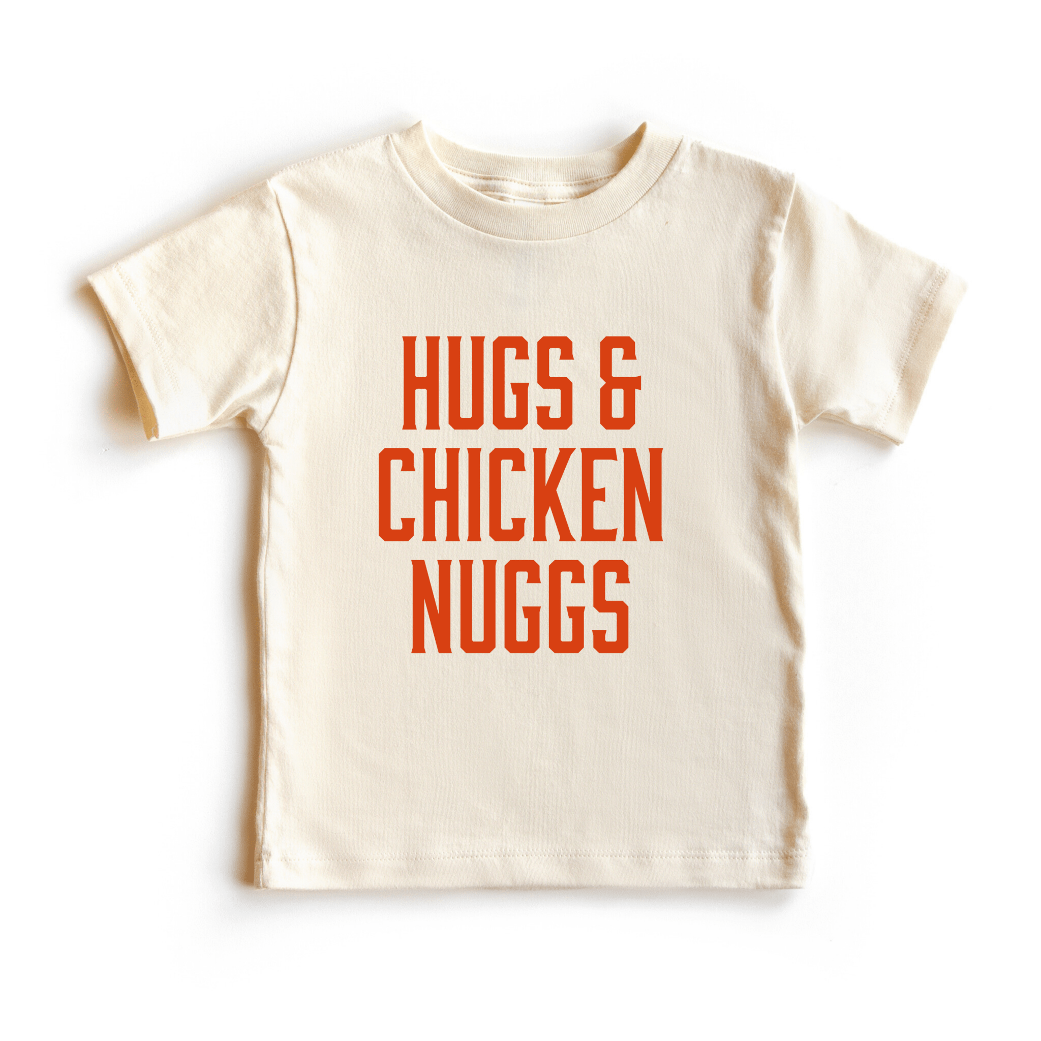 Chunky Deli toddler tee in 100% cotton, short sleeve, beige/natural color with bold orange block text reading 'Hugs & Chicken Nuggs' across the chest. Playful foodie apparel for kids.