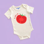 White baby onesie with red tomato graphic and text on a purple background