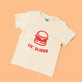 Chunky Deli product image: Toddler tee in 100% cotton, short sleeve, beige/natural color. Features a graphic illustration of a burger with the text "Lil' Slider" underneath, centered on the chest on a pastel orange background.