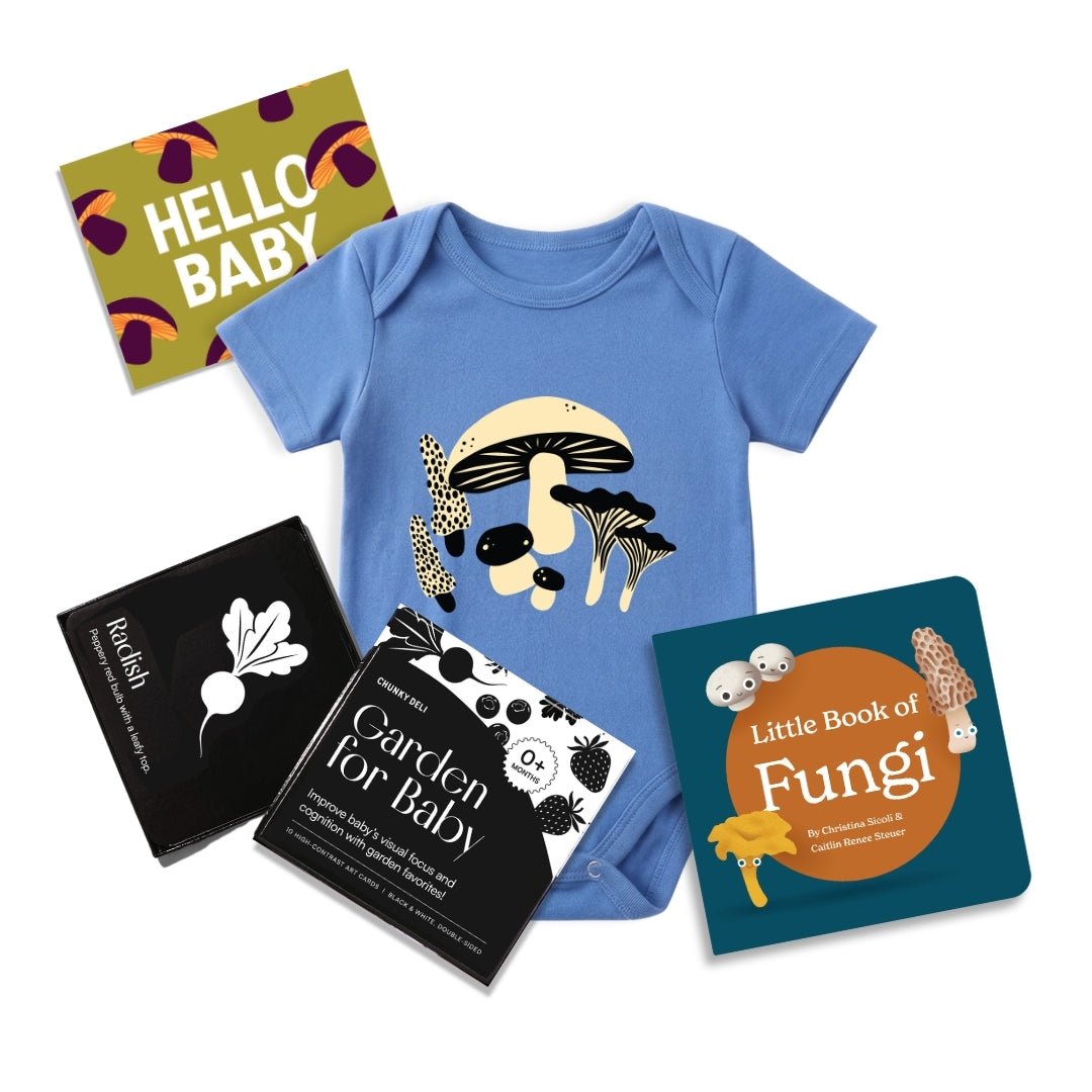 Flat lay product image features blue mushroom baby bodysuit, black and white high contrast garden for baby art cards, little book of fungi and a "hello Baby" gift note. 