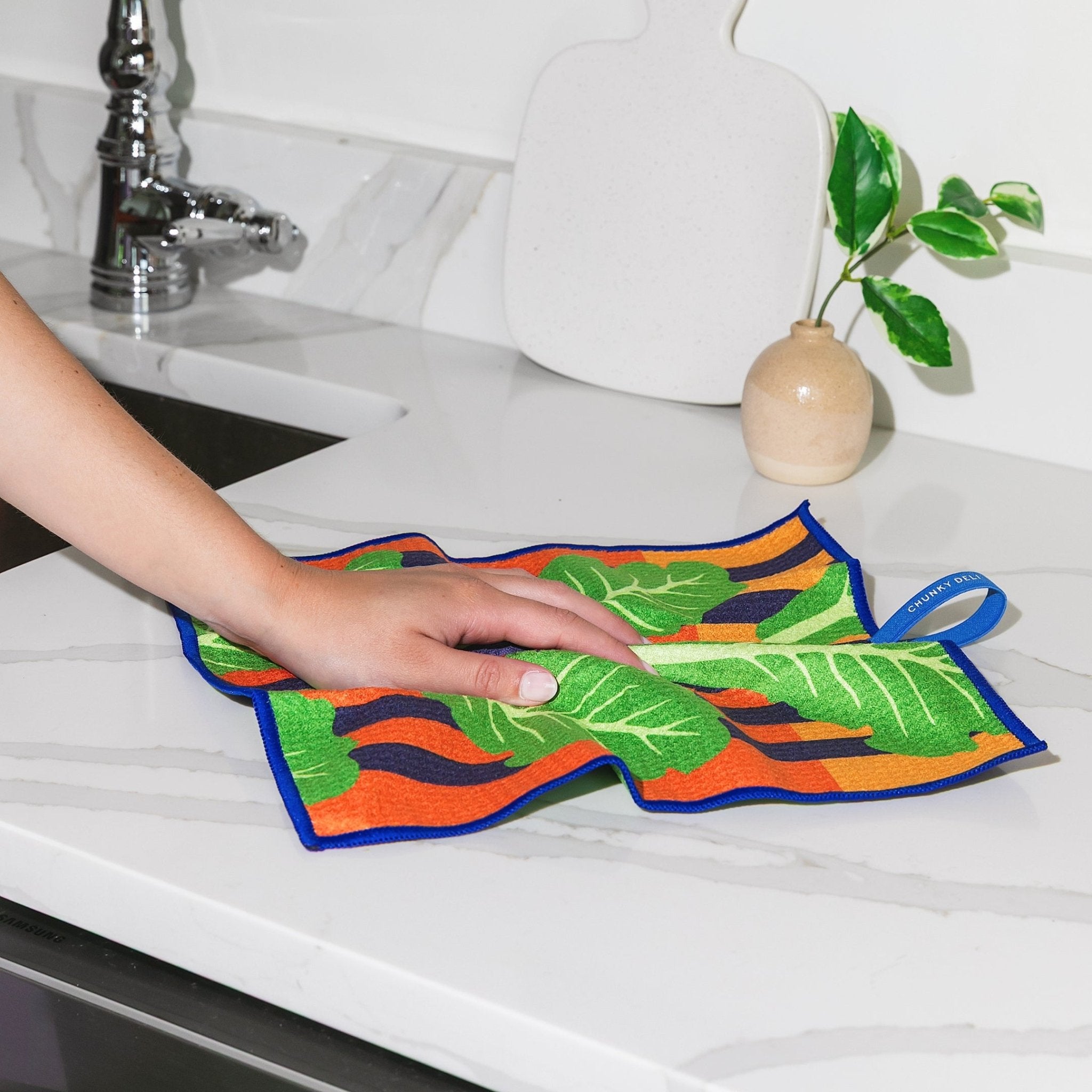 Chunky Deli Product image of a person holding a colorful romaine leaf-patterned cleanup cloth on a kitchen counter.