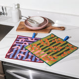 Chunky Deli product image with two patterned pot cleanup cloths on a kitchen counter with utensils and a cutting board. Featuring two designs; Tomato and shirmp. 