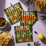 Chunky Deli lifestyle image of a Set of three green potholders with colorful lemon and olive pattern on a purple surface with bread and olives.