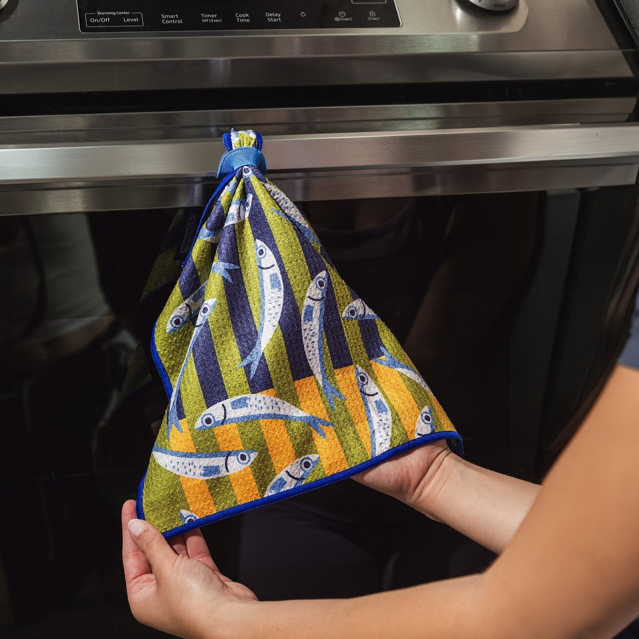 Chunky Deli product image of a person holding a colorful anchovy fish-patterned cleanup cloth in front of an oven.