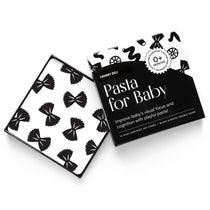 High-angle product shot of a black and white "Pasta for Baby" art card set. A card with a bow tie pasta pattern rests on the open box.