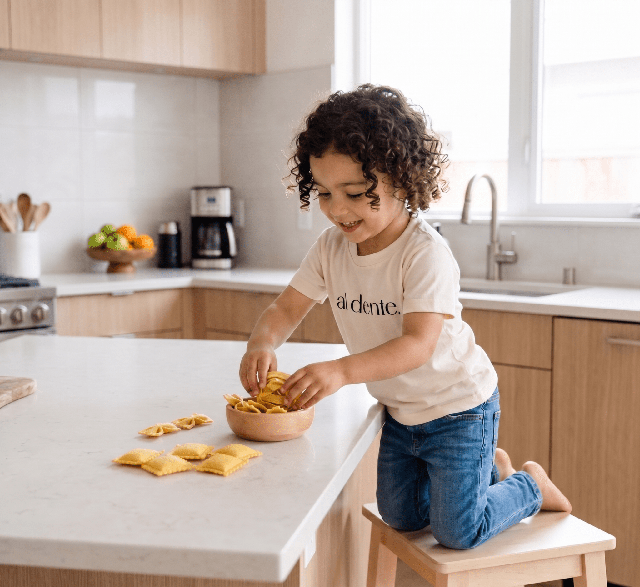 Child playing with felt pasta on a kitchen counter, wearing Al Dente Kids' Tee from Chunky Deli.