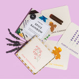 Chunky Deli product image: "Spice Rainbow" art cards box open on a purple background, with spice cards scattered around, showcasing illustrations and sight words. Real lavender sprigs are included to highlight the connection to the lavender card and its e