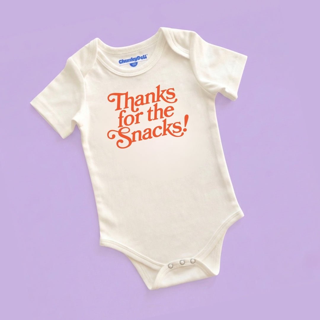 Product display image of the "Thanks for the Snacks!" baby bodysuit in natural cotton, laid flat on a pastel purple background. Chunky Deli product image.